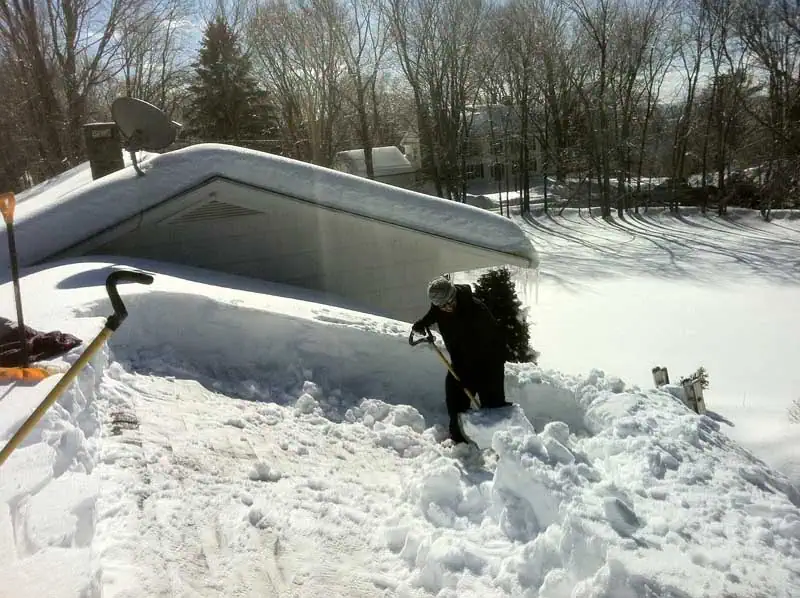 Man on roof shoveling three feet of snow.