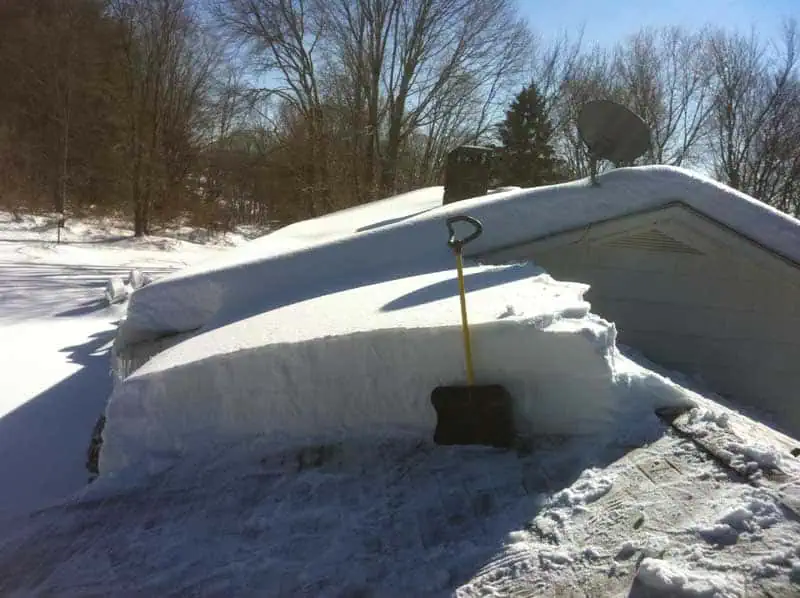Shovel in front of a wall of at least4 feet of snow on a roof.