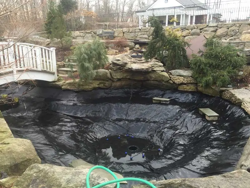 A new koi pond being lined with waterproof sheet, with a white walking bridge in the background.