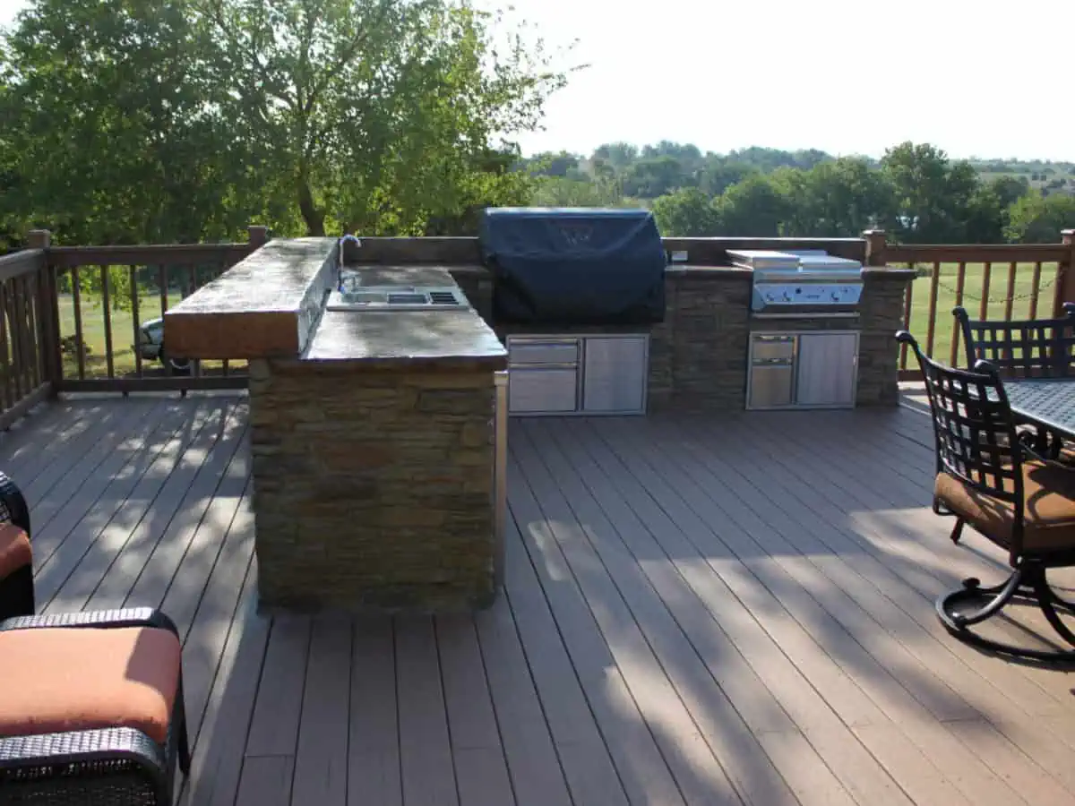 Outdoor kitchen with grill and refrigerator on a deck.