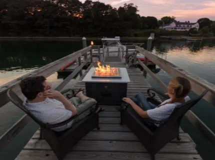 Fire table on the dock with man and woman in adirondack chairs.
